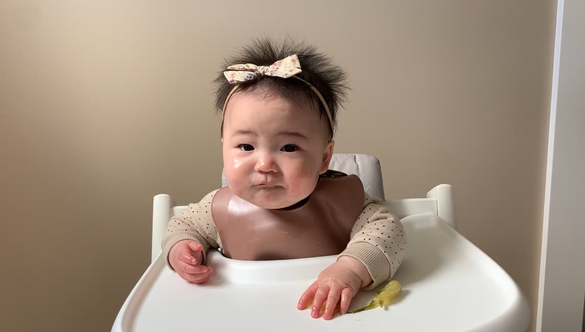 a landscape photograph of a baby looking toward the camera in their high chair, not eating food that's lying on the tray